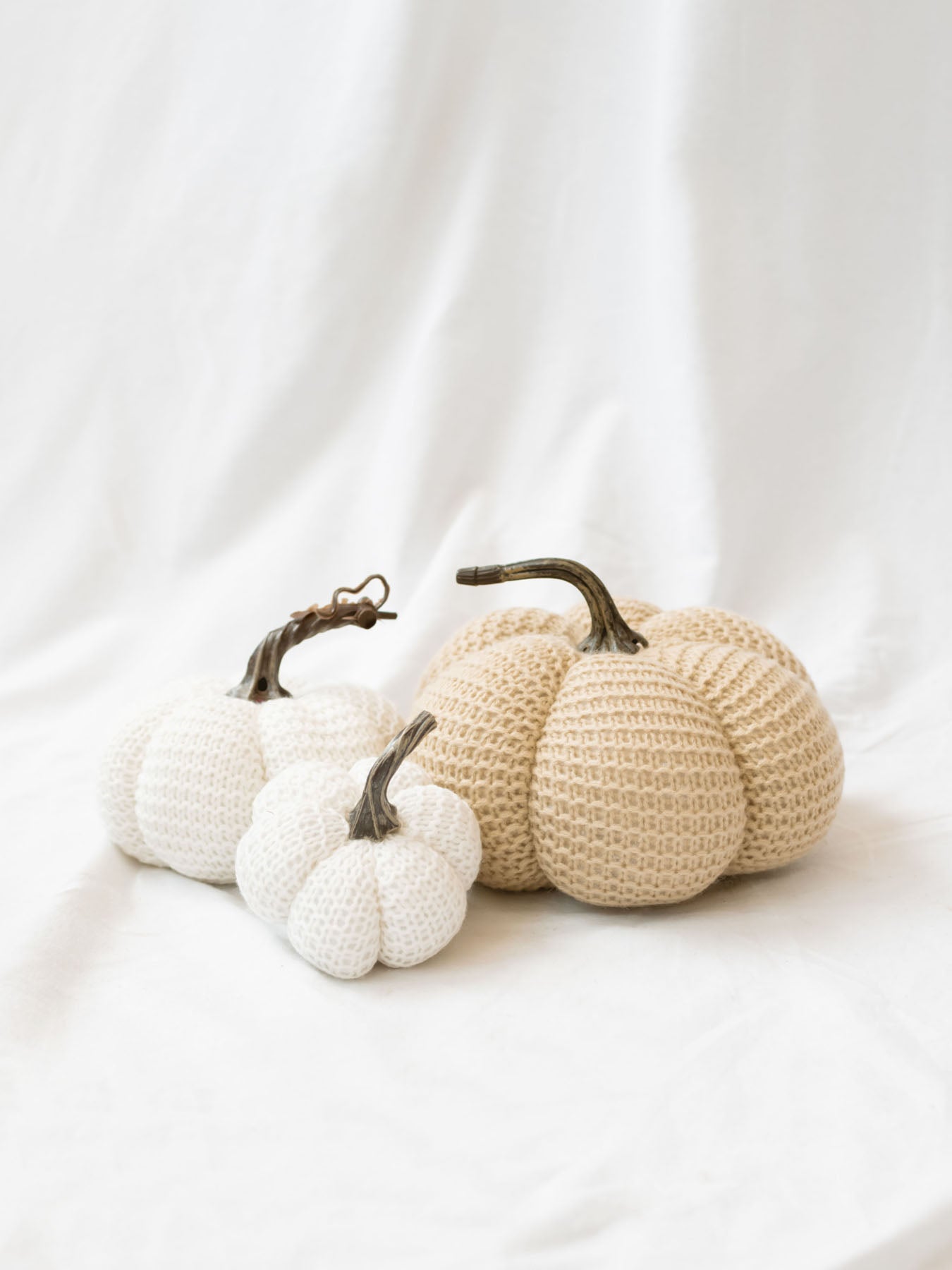 Tan and white knit pumpkins sitting on white linen backdrop. 