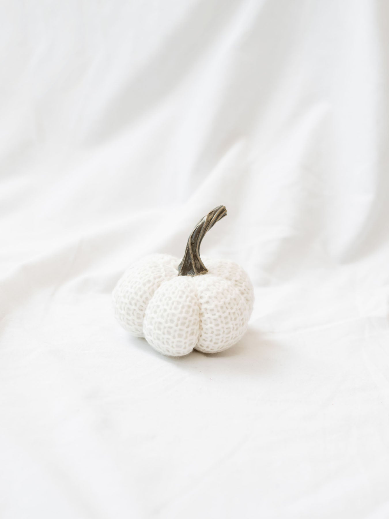 Small size knit stuffed white pumpkin on white linen backdrop. 