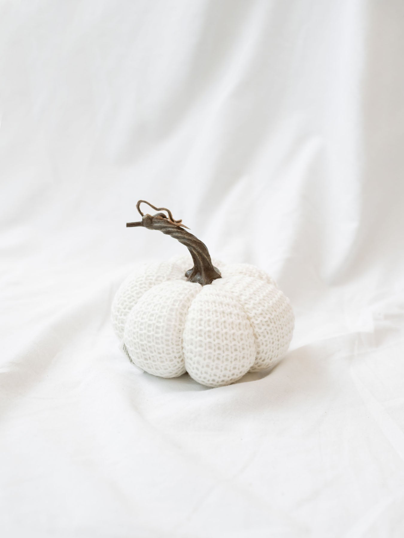 Large size knit stuffed white pumpkin on white linen backdrop. 