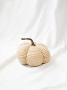 Tan knit stuffed pumpkin sitting on white linen backdrop. 