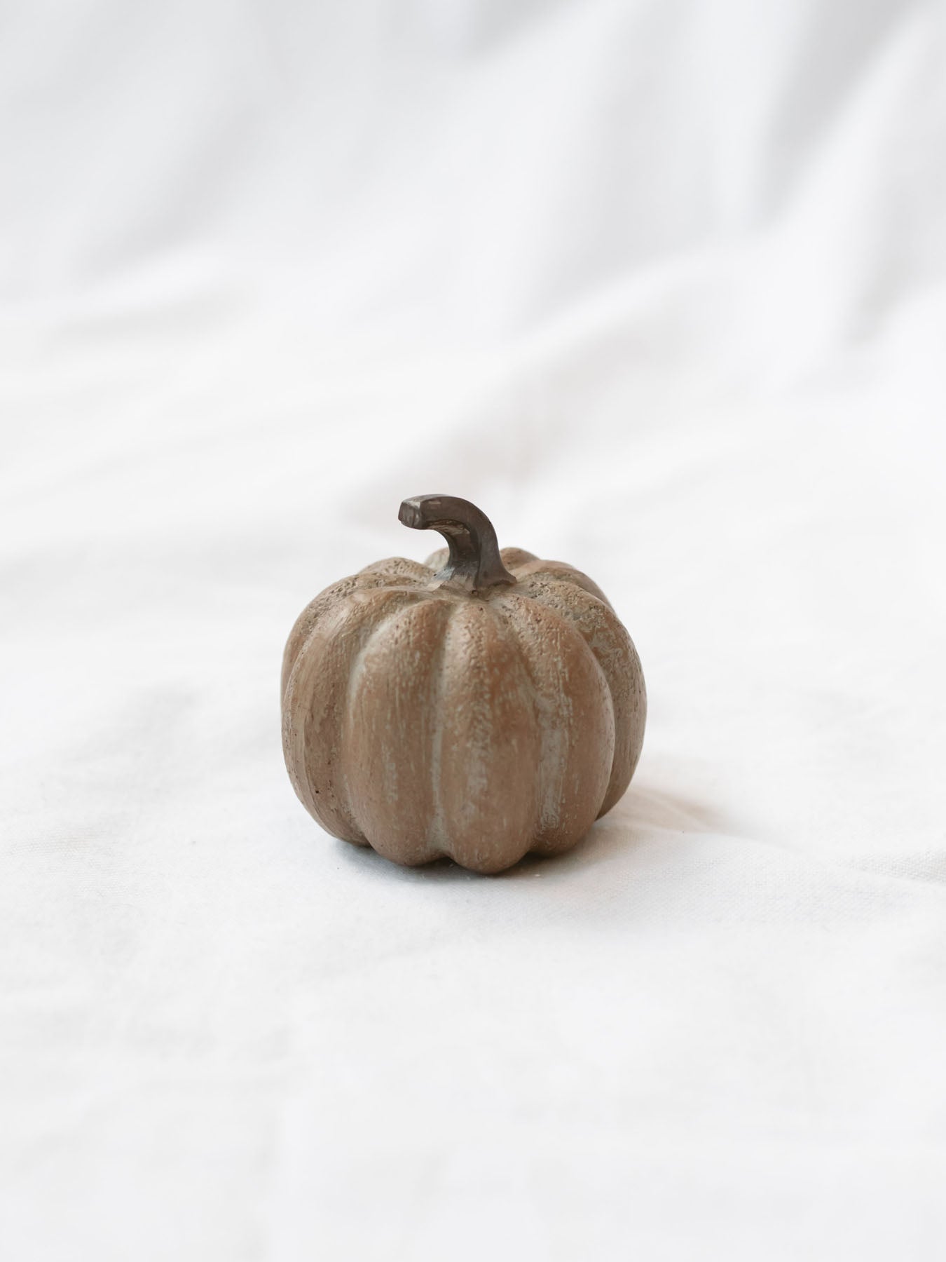Small brown wood grain pumpkin sitting on white linen backdrop.