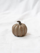 Small brown wood grain pumpkin sitting on white linen backdrop.