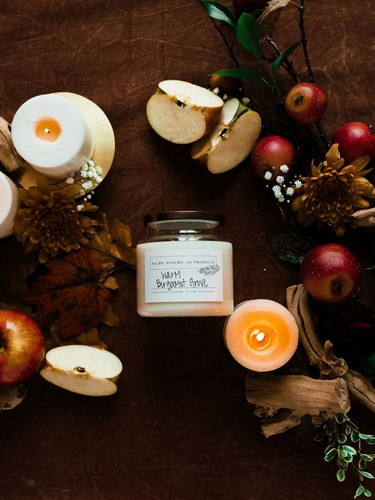 Warm Bergamot Grove candle on a brown background with candles, apples and other fall florals