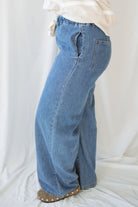Woman wearing wide leg medium wash denim with drawstring waistband with taupe sweatshirt on a white background.