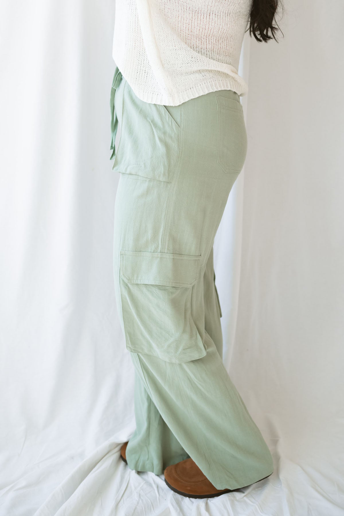Woman wearing sage green relaxed wide-leg utility pants with oversized cargo pockets and an adjustable drawstring waist.