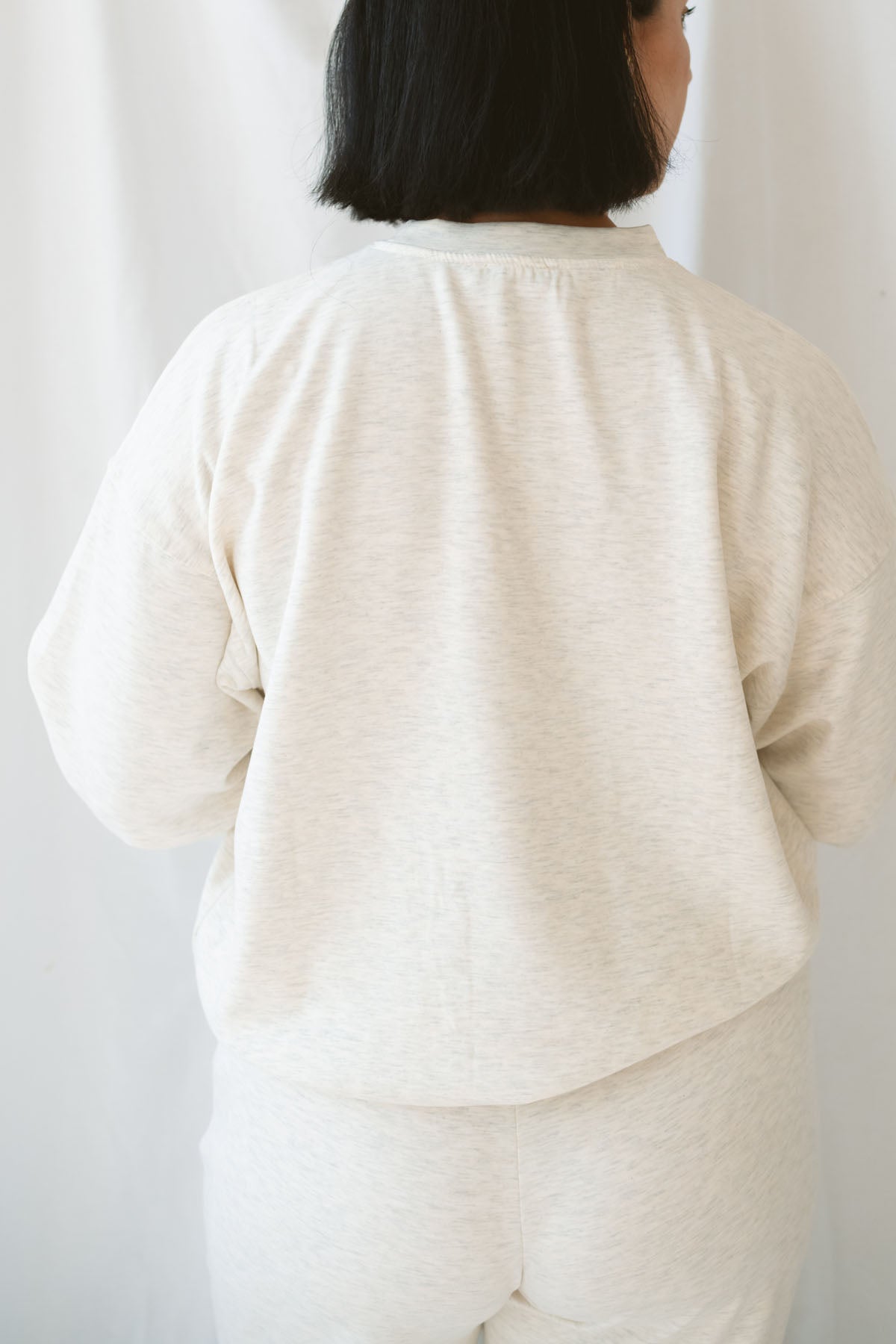 Woman wearing a light beige lounge set with crew neck sweatshirt and drawstring pants on a white background 