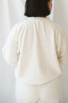 Woman wearing a light beige lounge set with crew neck sweatshirt and drawstring pants on a white background 