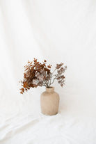 Brown eucalyptus bundle sitting in small vase against white linen backdrop.